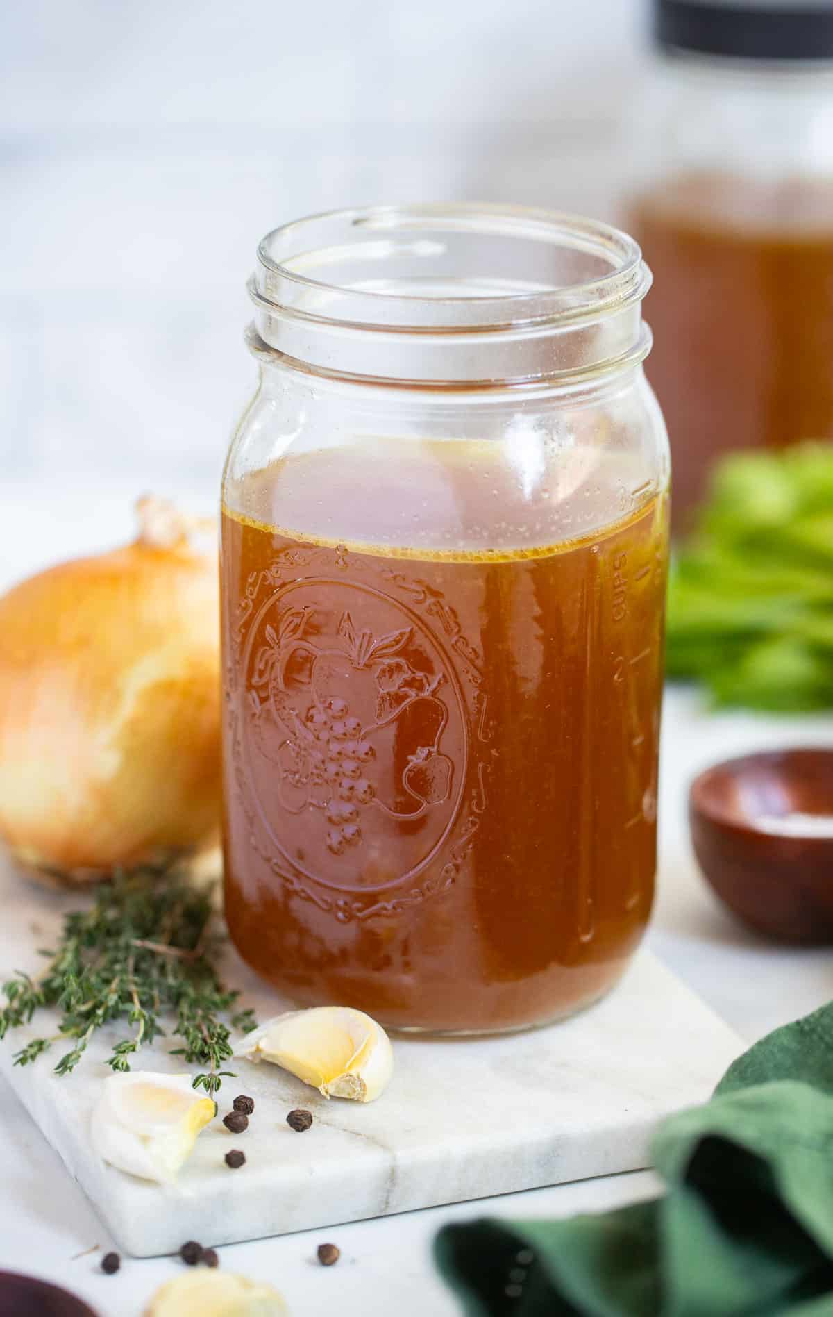 slow cooker chicken broth in clear mason jar on counter with ingredients arranged around it