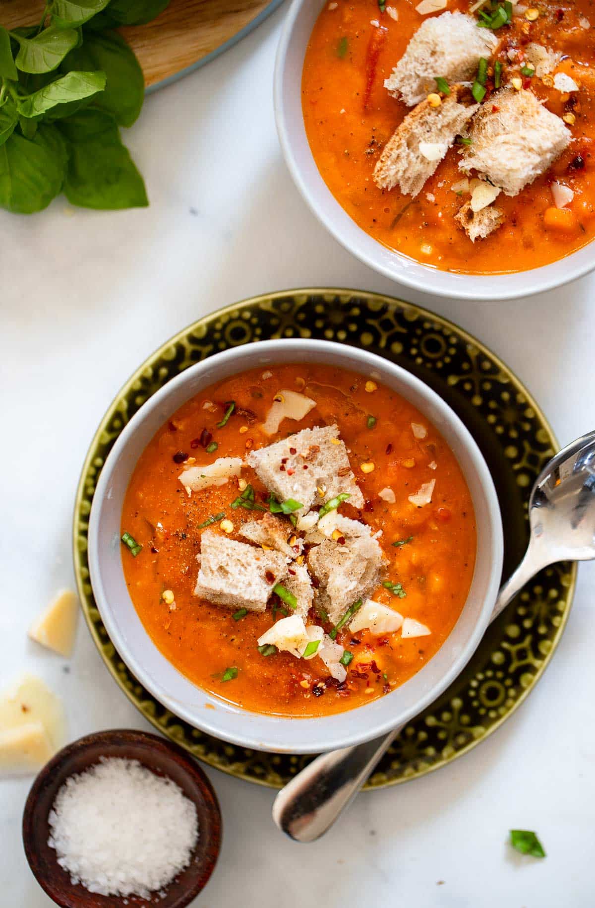 two bowls of tuscan tomato soup with garnishes on white counter background