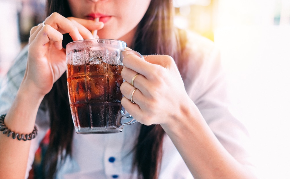 Close up of a woman drinking cola in a glass with a straw.