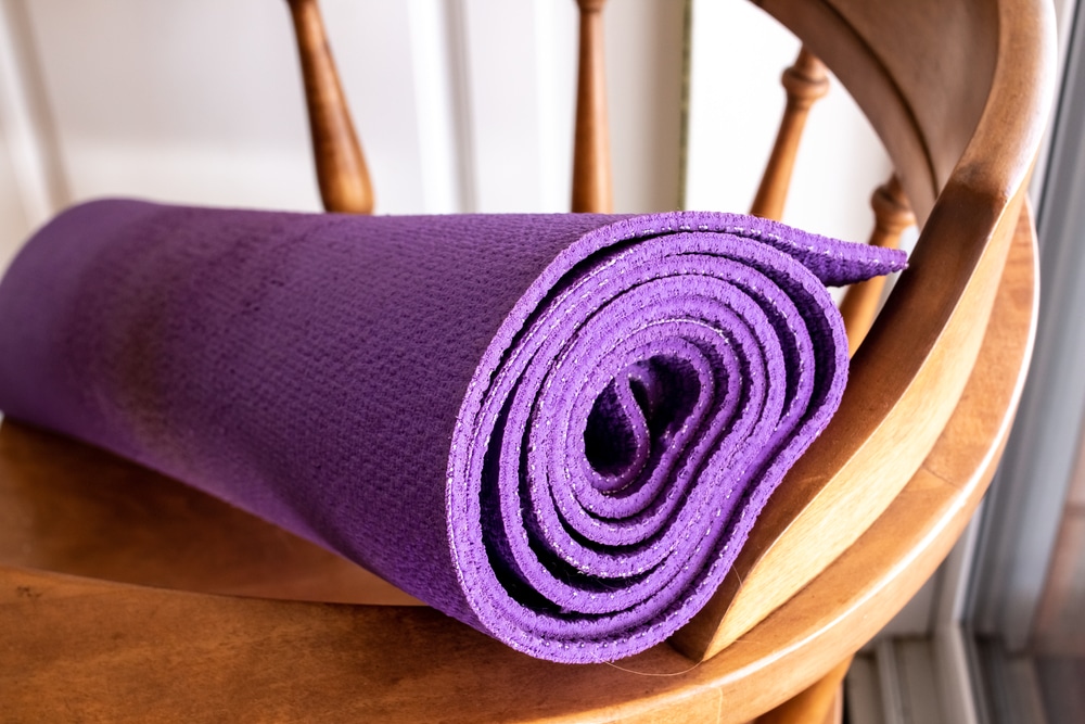 A rolled up purple yoga mat on a wooden chair.
