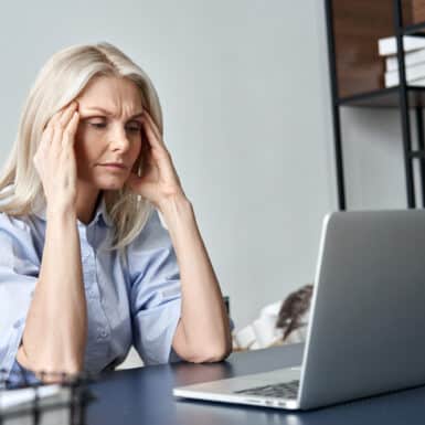 A woman with a headache while sitting at her desk in front of the computer.