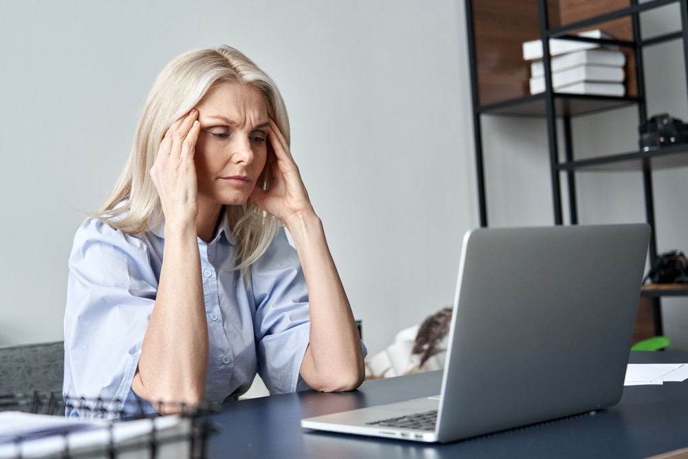 A woman with a headache while sitting at her desk in front of the computer.