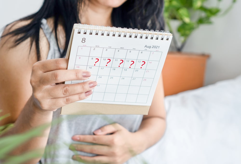 Woman holding her stomach and a calendar with question marks.