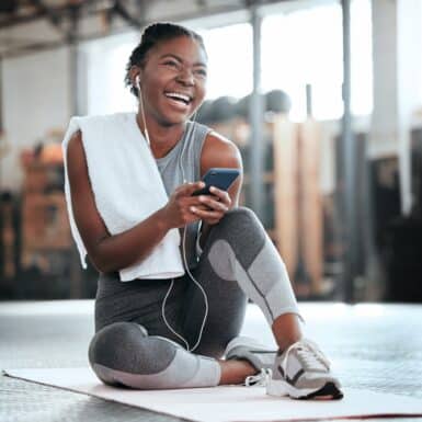 A woman laughing at her phone while taking a break from exercising at the gym.
