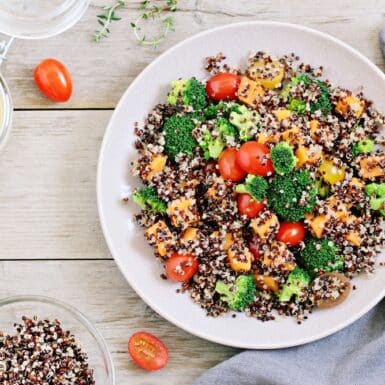 Quinoa salad with broccoli, sweet potatoes and tomatoes on a rustic wooden table.