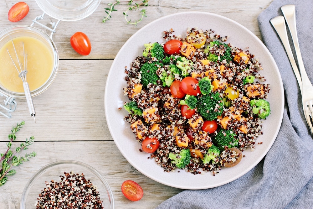 Quinoa salad with broccoli, sweet potatoes and tomatoes on a rustic wooden table.