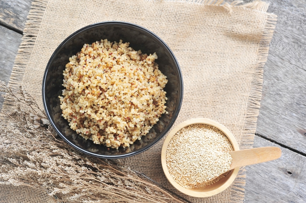 Cooked quinoa in a bowl next to a smaller bowl of uncooked quinoa.