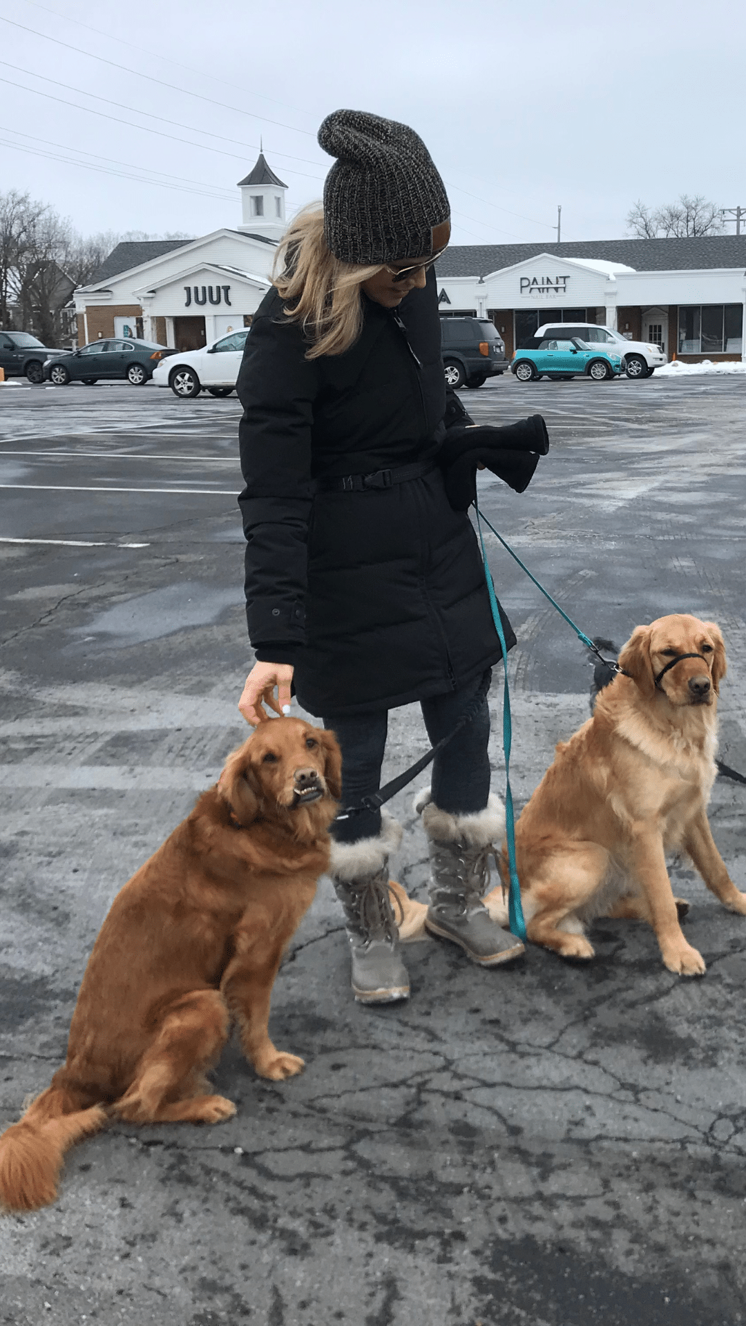 Chris Freytag wearing a black long winter jacket with 2 golden retriever puppies on a leash. Standing in a parking lot.