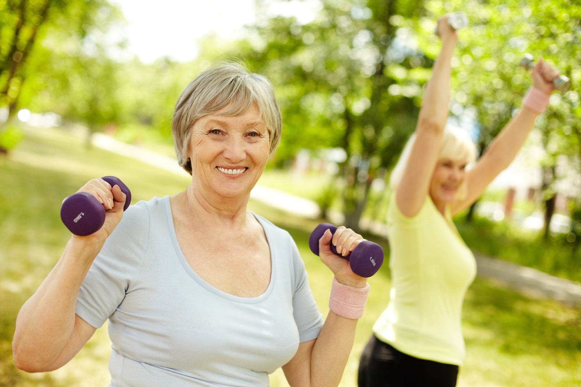Smiling older woman doing dumbbell exercises outside.