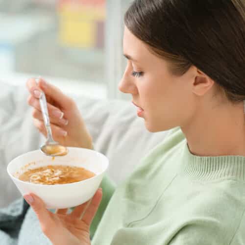 Sick young woman eating chicken noodle soup at home.