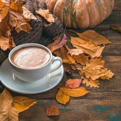 A cup of coffee, foliage, pumpkin, and a sweater on a wooden background.