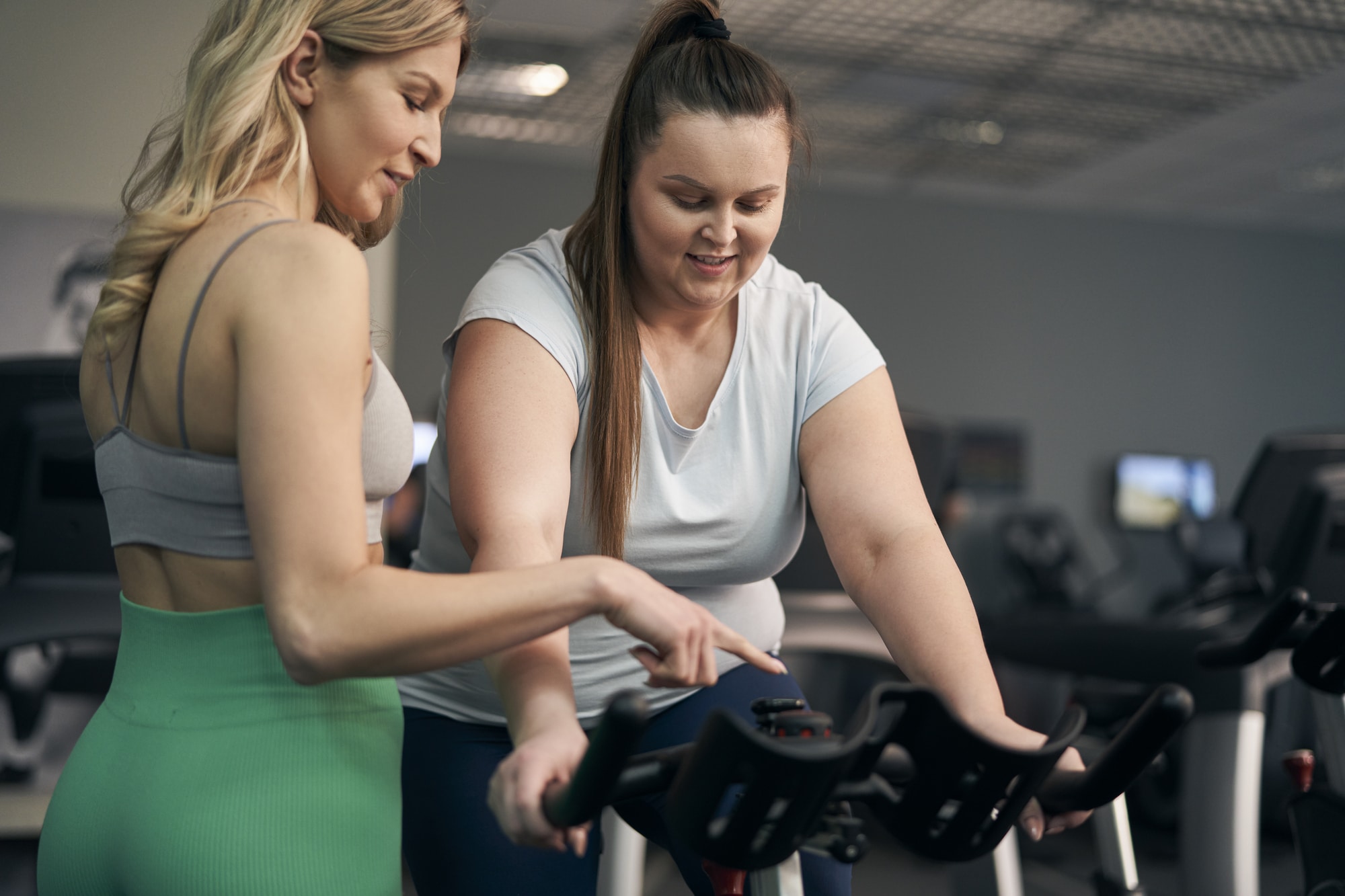 Instructor helping plus size woman on a stationary bike at the gym.