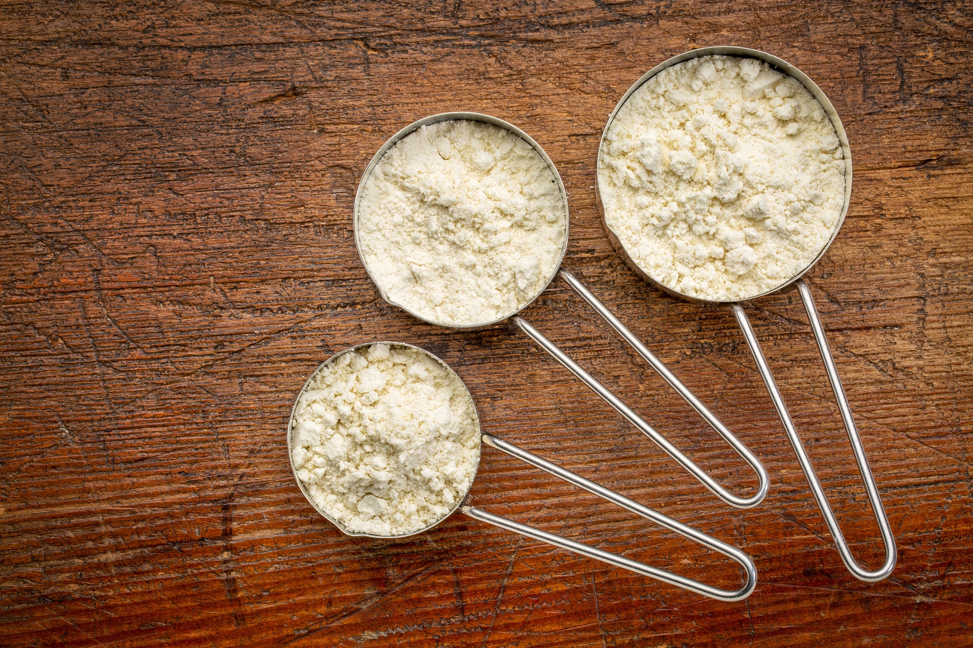 Measuring metal scoops of whey protein powder against rustic grunge wood.