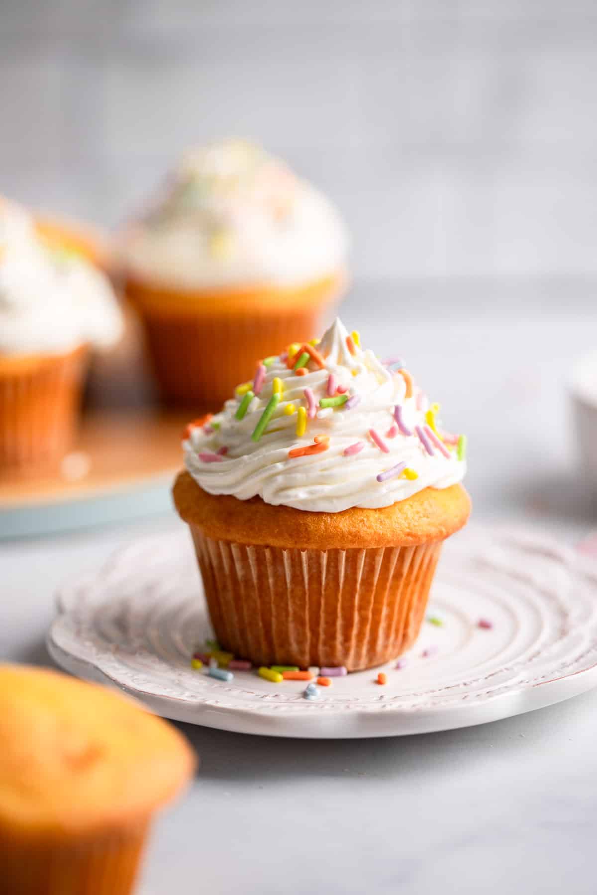 vanilla cupcake on white place with healthy cream cheese front and colorful sprinkles