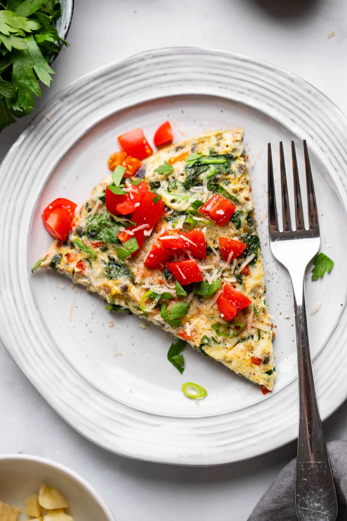top view of single serving of healthy vegetable frittata on white plate with fork