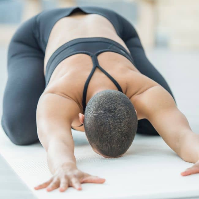 woman in childs pose wearing black two piece outfit on yoga mat
