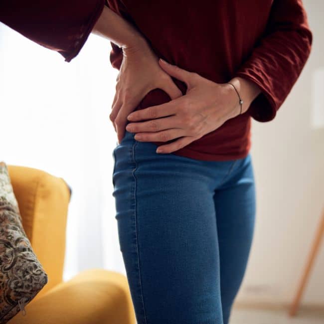 woman holding her hip in pain with two hands wearing jeans and sweater