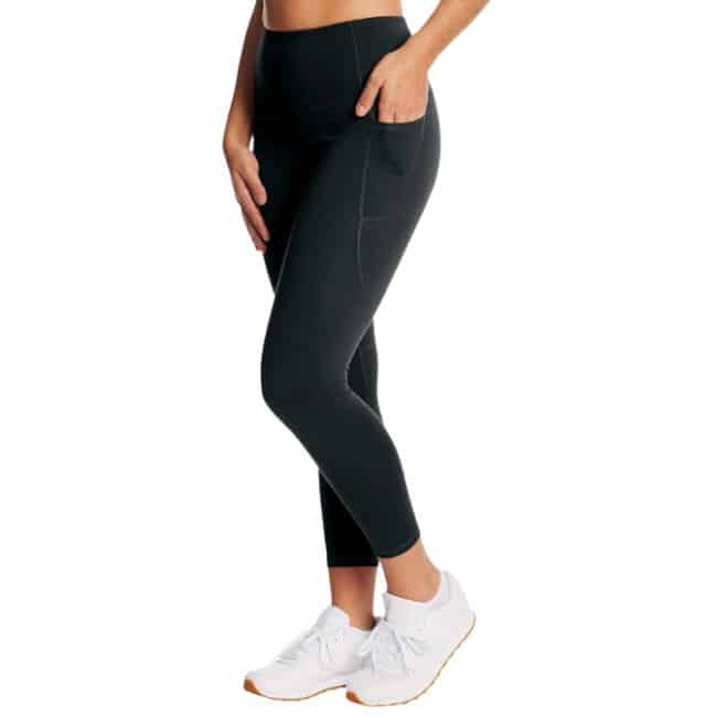 bottom half of woman wearing black leggings with hand in pocket and white tennis shoes
