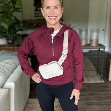 Chris Freytag wearing a maroon quarter zip sweatshirt with a tan cross body bag. Modeling her outfit with flare leggings on.