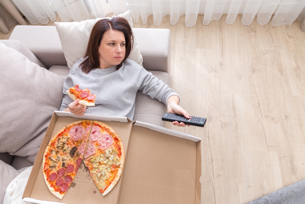 Overhead view of a woman eating an entire box of pizza while watching TV.