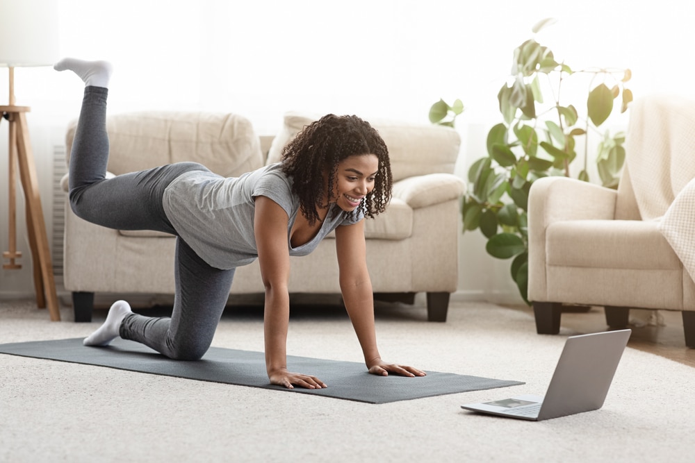 Woman doing a leg workout at home while looking at a laptop.