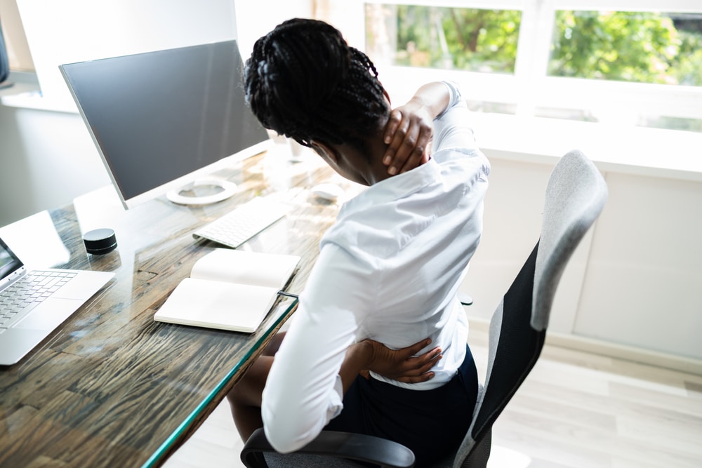 A woman massaging her neck at an office desk.