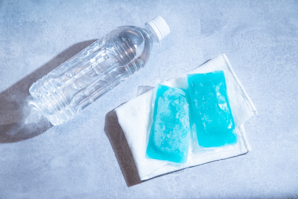 Two blue ice packs on top of a white towel next to a bottle of water.