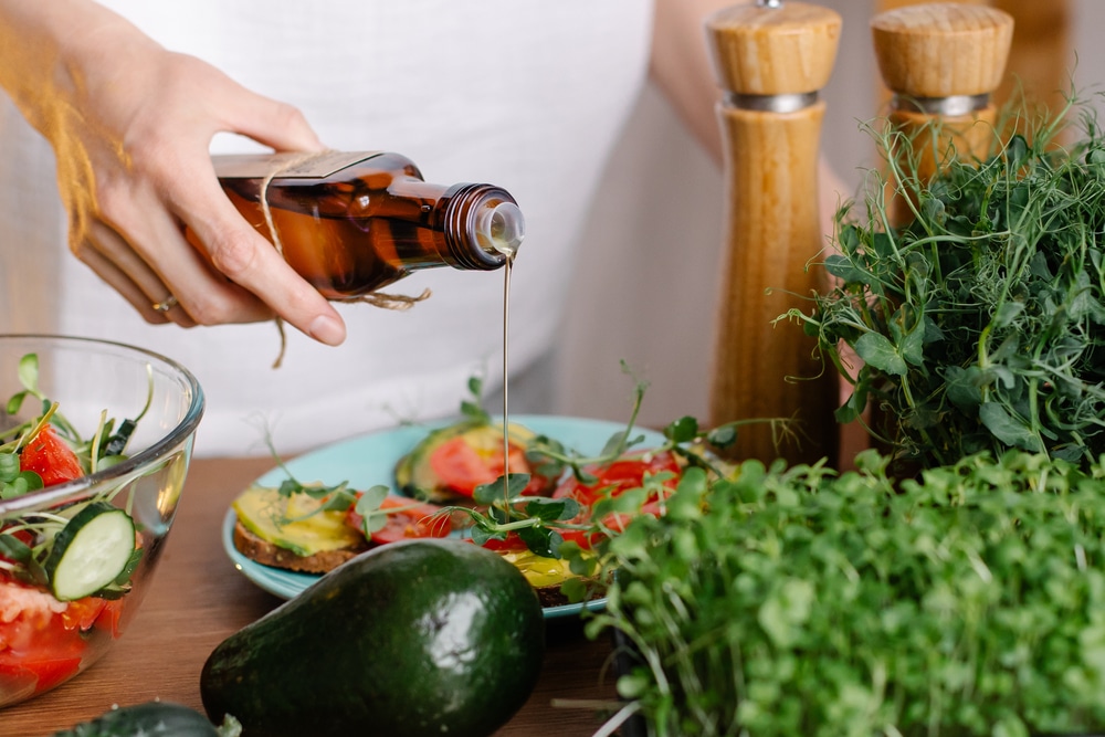 A hand pouring olive oil over top of a healthy salad.