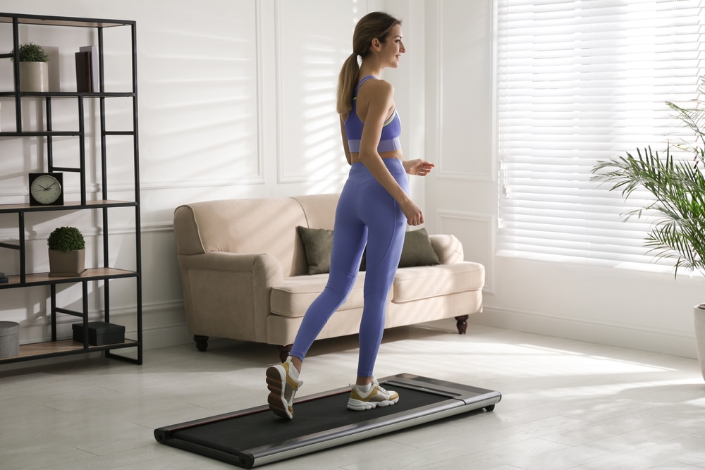 A woman walking on a walking pad treadmill in her living room.