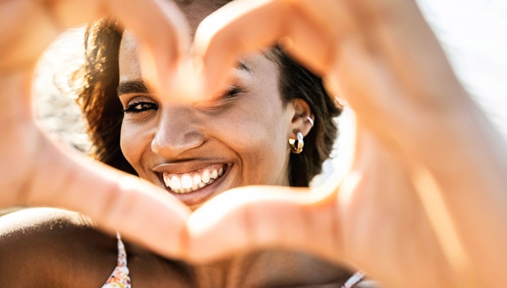 Close up of a woman smiling and making a heart shape with her hands.