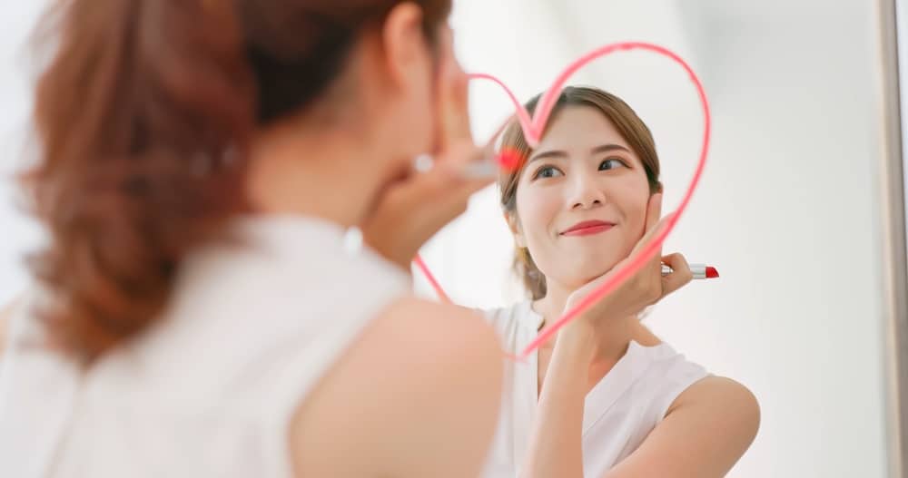 A woman smiling at her reflection in the mirror with a heart drawn around it.