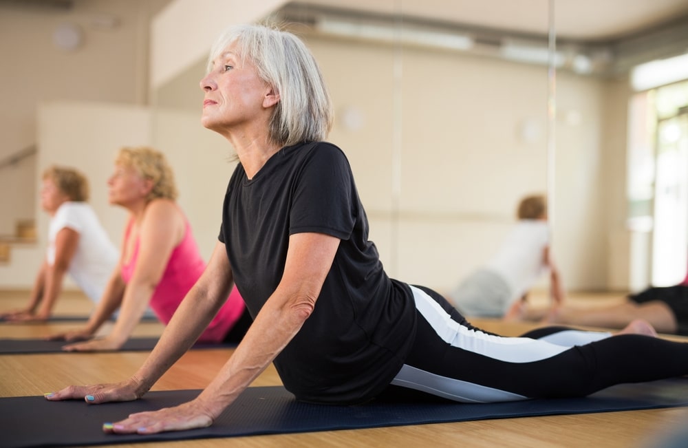 Older woman doing a cobra pose in a group yoga class.
