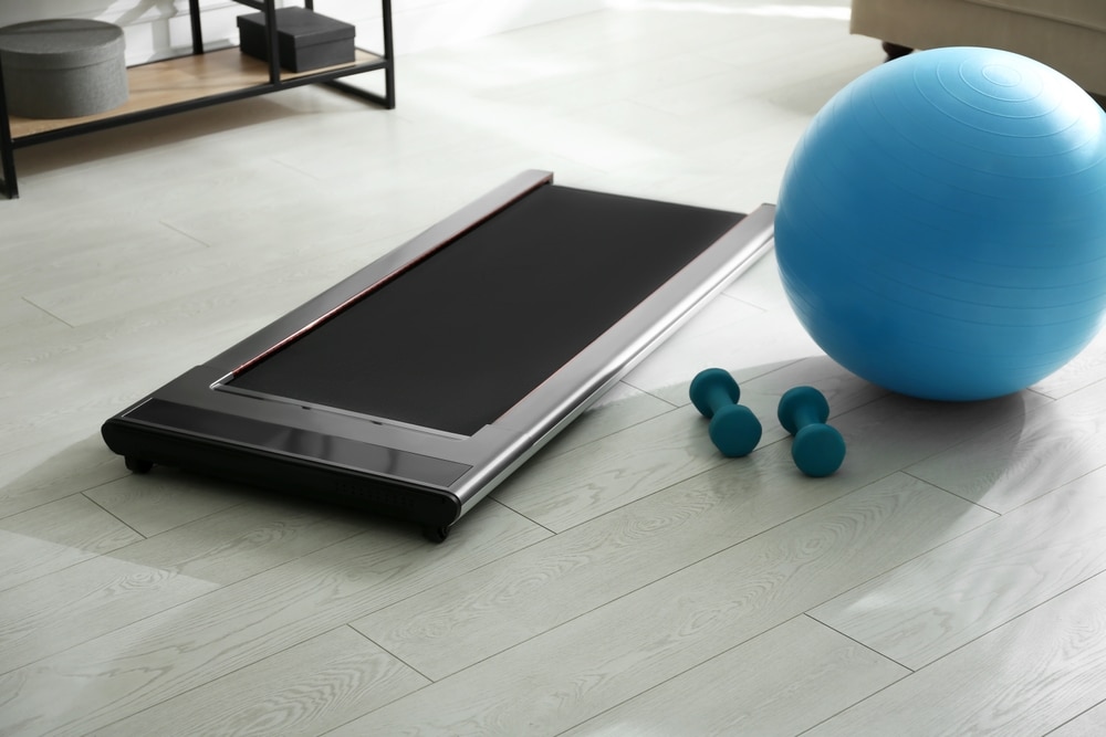 A walking pad treadmill next to small dumbbells and a workout ball.
