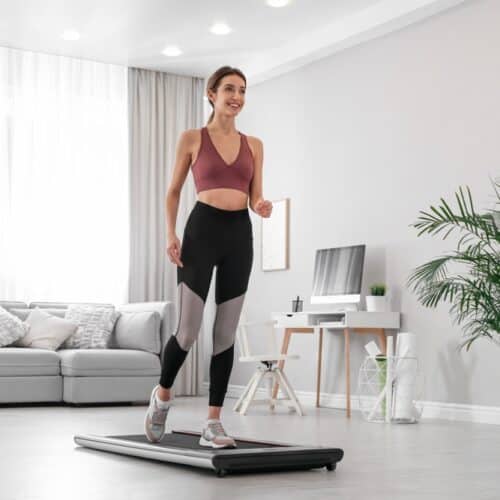 A woman smiling while walking on a walking pad treadmill in her living room.