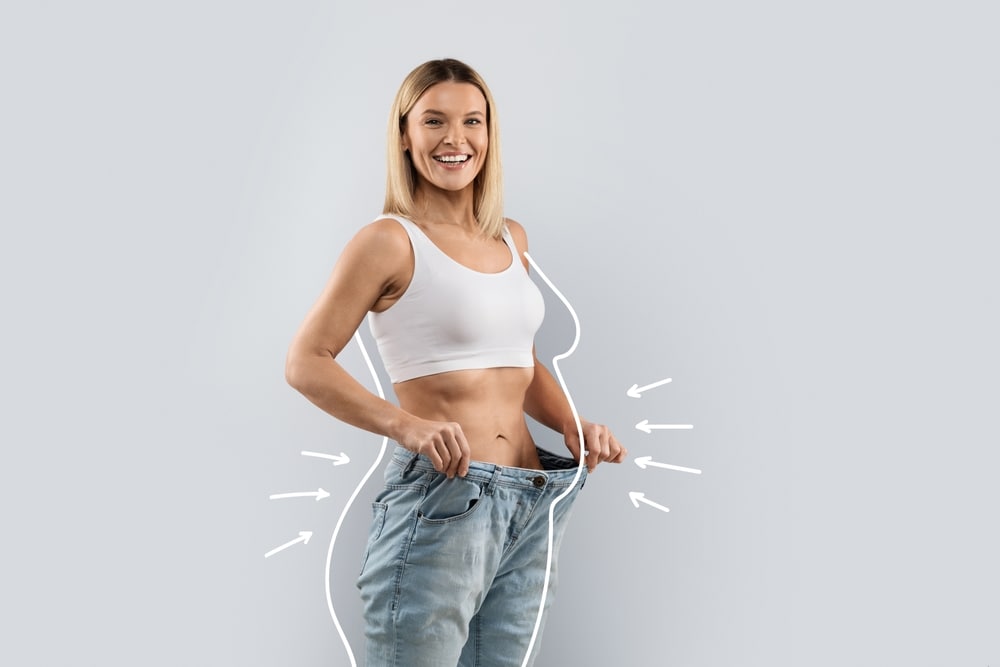 A middle aged blonde woman wearing huge jeans, showing weight loss.