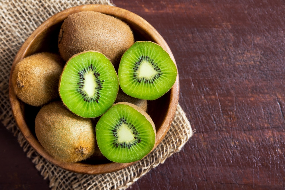 Kiwifruit cut in half in a wooden bowl on a wooden background.