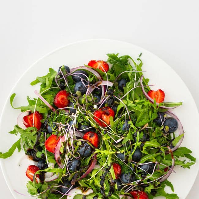 berry arugula salad on white plate on white counter