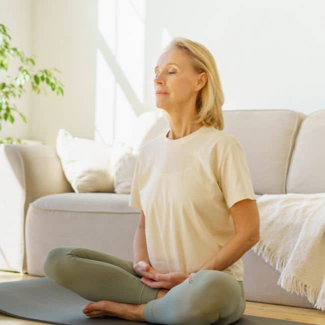woman sitting cross legged relaxing and mediating to improve brain fog symtpoms