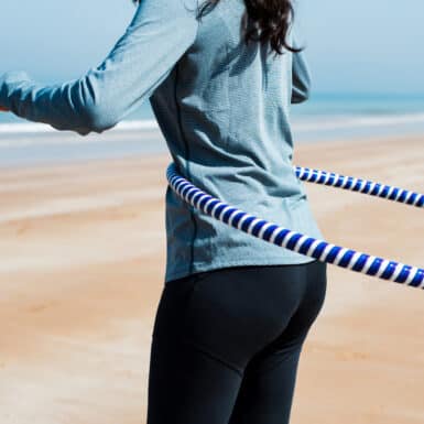 Girl exercising with hula hoop on the beach.