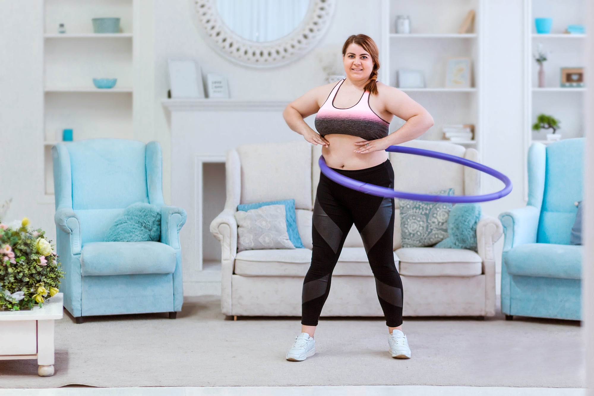 A plus-size woman exercising with a weighted hula hoop in her living room.