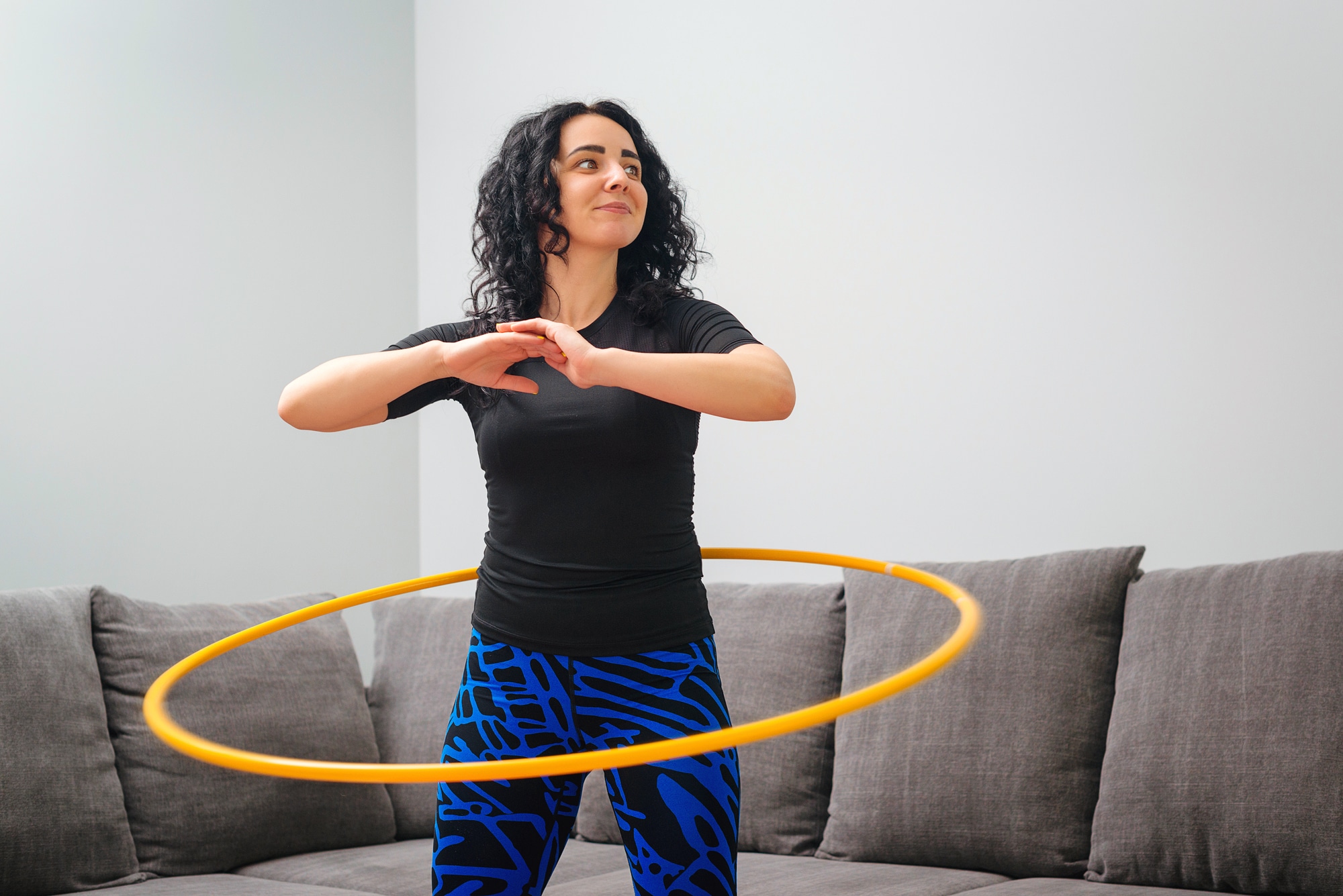 Woman exercising using a weighted hula hoop in her living room.