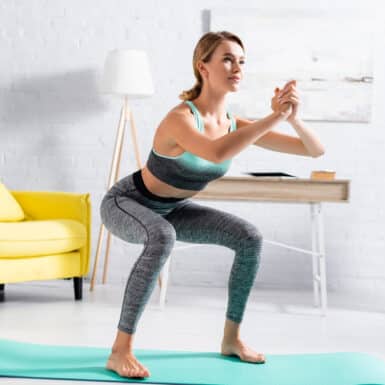 A woman doing squats on a teal yoga mat in her living room.