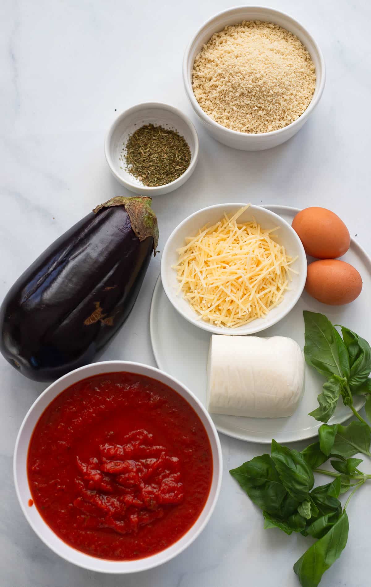 overhead view of raw ingredients to make healthy eggplant parmesan on white countertop