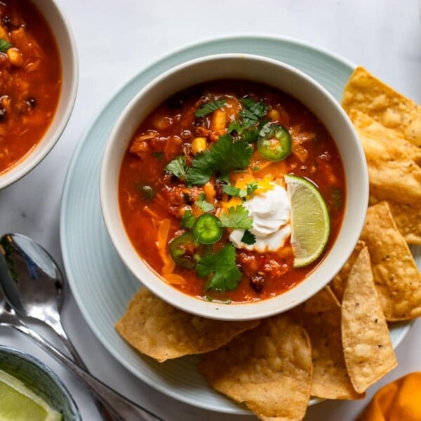 overhead view of single serving of low calorie southwestern chicken soup with sides on white counter backdrop