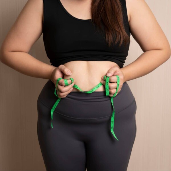 woman holding tape measuring over belly ready to do exercises to get rid of apron belly