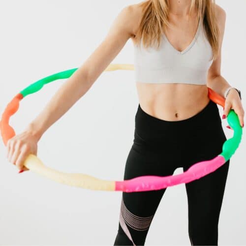 woman standing from neck down with colorful weighted hula hoop around waist