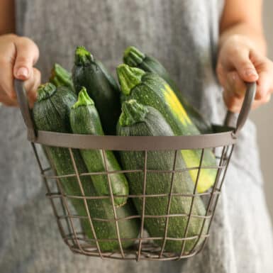 woman holding metal basket of large zucchinis