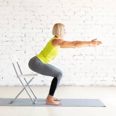 Older woman doing chair squats on a yoga mat.