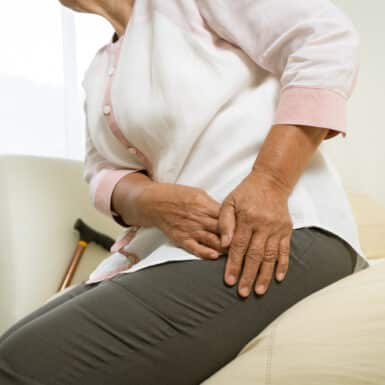 An older woman massaging hip pain while sitting on a bed.