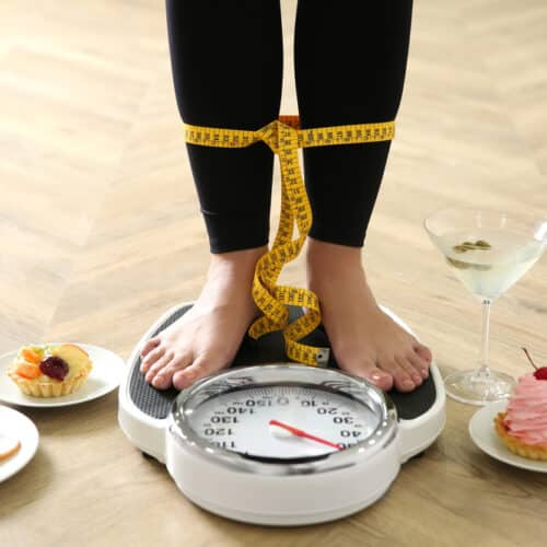 A woman's feet on a floor scale depicting holiday weight gain from various foods and drinks.